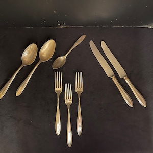May include: A set of vintage silverware, including two spoons, three forks, and two knives. The silverware is made of silver and has a polished finish.