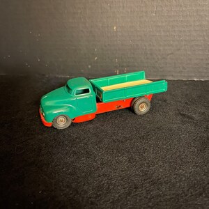 May include: A green and red toy truck with a flatbed. The truck has a white bed and black wheels.