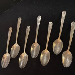 May include: Set of eight silver spoons with engraved images of historical figures. The spoons have a traditional design with a rounded bowl and a long, slender handle.