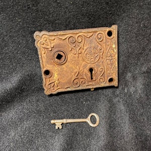 May include: A rusty metal door lock with an ornate design and a keyhole. The lock has a key with a simple design.