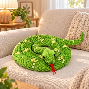 Peut inclure: Un serpent en peluche enroulé en forme circulaire, doté d'un tissu vert texturé avec un motif répétitif de petites taches jaunes. Le serpent possède des yeux en plastique noir et une longue langue plate en feutrine rouge vif.