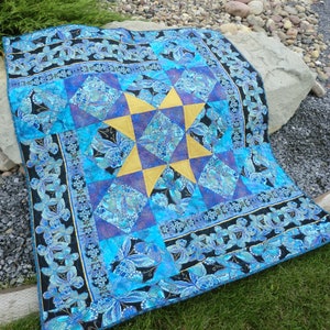 Puede incluir: Una colcha azul y dorada con un diseño de estrella y un borde con estampado de mariposas. La colcha está hecha de tela con un brillo metálico.