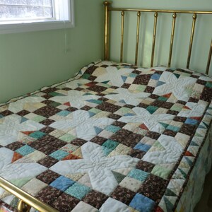 May include: A brass bed frame with a white and brown patchwork quilt. The quilt has a star pattern and is quilted with a decorative stitch.