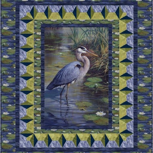 Könnte beinhalten: Ein blauer Reiher steht in einem Teich mit Seerosen und grünen Schilf. Der Reiher ist scharf gestellt, der Hintergrund ist verschwommen. Das Bild ist mit einem Rahmen aus grünen und blauen Dreiecken umrahmt.