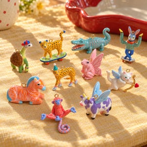 May include: A collection of ten small, colorful animal charms featuring a turtle with a cap, a leopard on a skateboard, a blue crocodile, a rabbit on a skateboard, a zebra, a leopard in a party hat, a pink fairy frog, a winged cat with a bow, a red monkey, and a winged cow.