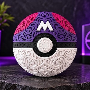 May include: A spherical object featuring a complex, raised filigree pattern. The top half is purple and pink, the bottom half is white, and a black band separates them. A white letter M sits at the top, and a circular white button is in the centre.