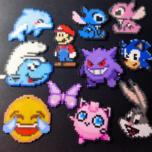 Peut inclure: Une collection de figurines en pixel art colorées réalisées avec des perles à repasser, incluant des personnages comme Mario, Sonic, Gengar, un Schtroumpf, un dauphin, un papillon, un émoji rieur et d'autres figures animées sur un fond sombre.