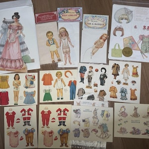 Puede incluir: Una colección de muñecas de papel de estilo vintage y conjuntos variados impresos en hojas de cartulina. El set incluye varias figuras, ropa de temporada, accesorios e ilustraciones de animales con etiquetas de texto como Mein Liebling y The A. Marque.