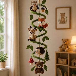 May include: A hanging mobile featuring a green crocheted spiral adorned with small crocheted figures including an owl, a fox, a deer, a hedgehog, a bear, a mushroom, an acorn, a pine tree, and green leaves, finished with a gold bell at the bottom.