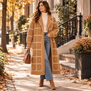 May include: A long, tan, open-front crochet cardigan featuring a grid pattern of white lines, worn over a cream-colored turtleneck sweater and blue denim jeans, paired with tan ankle boots and a small brown leather handbag.