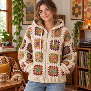Può includere: Una giacca con cappuccio e cerniera realizzata con quadrati all'uncinetto granny color crema. Ogni quadrato presenta un motivo floreale centrale nei toni del giallo senape, rosa antico, verde salvia e prugna scuro, con polsini e orlo a coste.