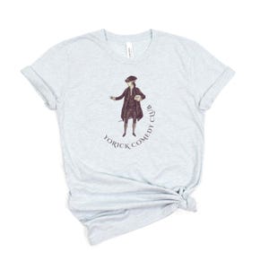 May include: Light blue t-shirt featuring a sepia-toned illustration of a man in historical attire. The image is encircled by the text "Yorick Comedy Club". The shirt is made of a soft material and has a classic crew neck.