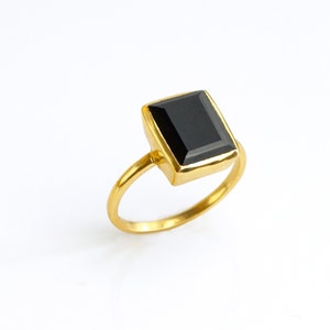 May include: A gold ring with a black square-shaped gemstone.