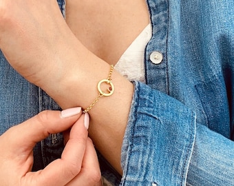 May include: A gold chain bracelet with a small circle charm. The charm has a small red stone in the center.