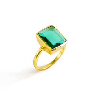 May include: A gold ring featuring a large, emerald green gemstone. The ring is set in a simple, square-shaped setting.