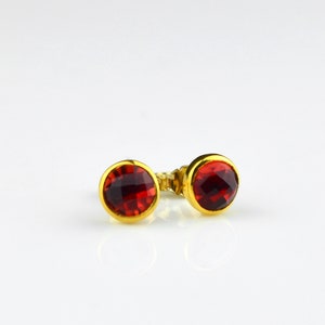 May include: A pair of gold stud earrings with red gemstone accents.