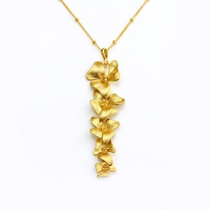 May include: A gold necklace with a pendant featuring a cluster of five delicate, gold-toned flower charms. The flowers are arranged vertically, creating a cascading effect.