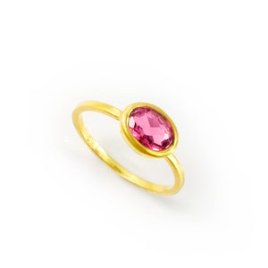 May include: A gold ring with a pink oval gemstone set in a bezel setting.