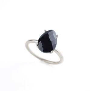 May include: A silver ring with a black gemstone set in a prong setting.