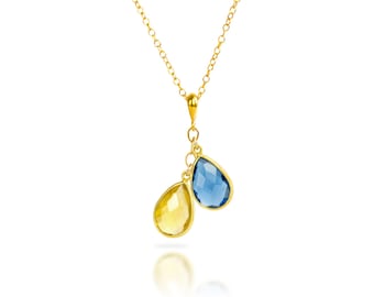 Könnte beinhalten: Eine goldene Kettenkette mit einem Anhänger mit zwei tropfenförmigen Edelsteinen. Ein Edelstein ist blau und der andere ist gelb.
