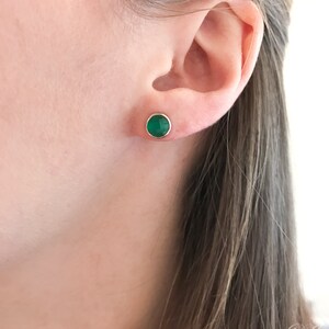 May include: A pair of gold stud earrings with a round green gemstone.