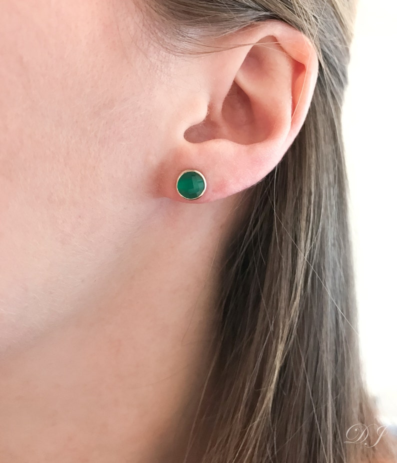 May include: A pair of gold stud earrings with a round green gemstone.