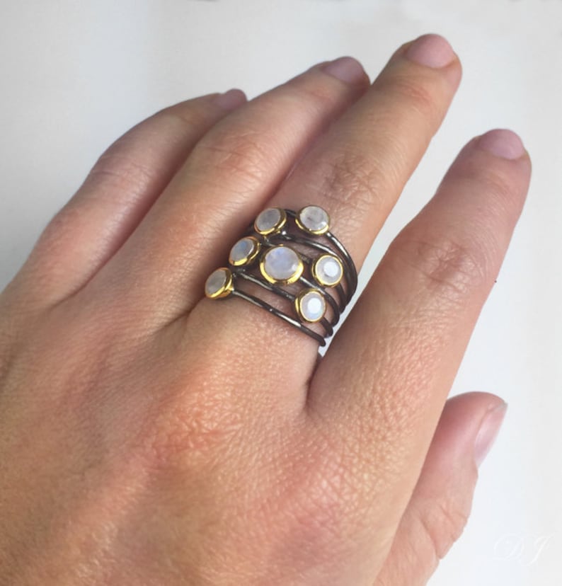 May include: A stack of seven silver rings with gold accents and moonstone gemstones. Each ring features a single round moonstone.