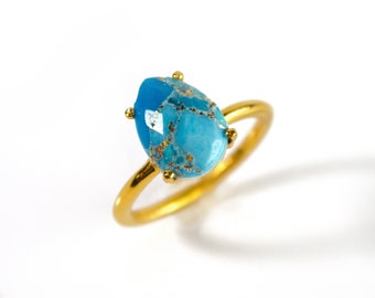 May include: A gold ring with a blue and gold gemstone. The gemstone is a teardrop shape and has a marbled pattern.