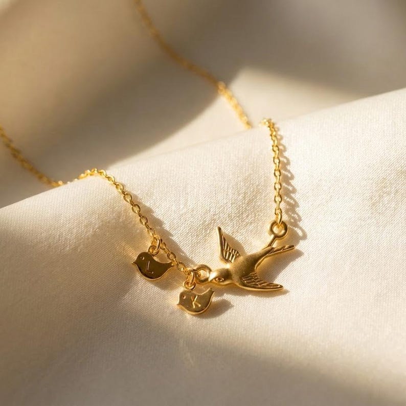 Gold mama bird necklace on linen with engraved initial baby bird charms, personalized family necklace for mom or grandma, meaningful motherhood jewelry gift.