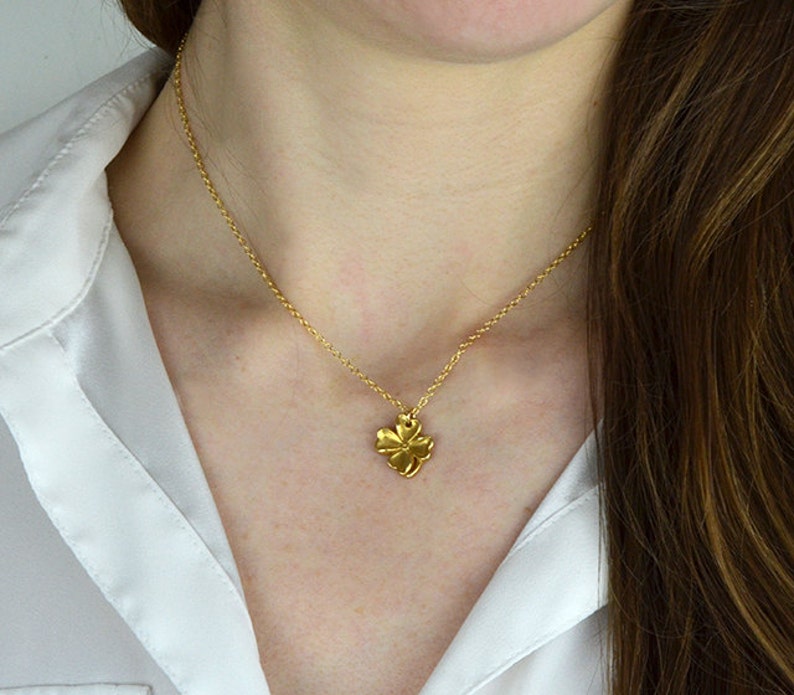 May include: A gold chain necklace with a small, gold, four-leaf clover pendant.