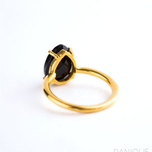 May include: A gold ring with a black pear-shaped gemstone. The ring is set with a simple band and the gemstone is set in a prong setting.