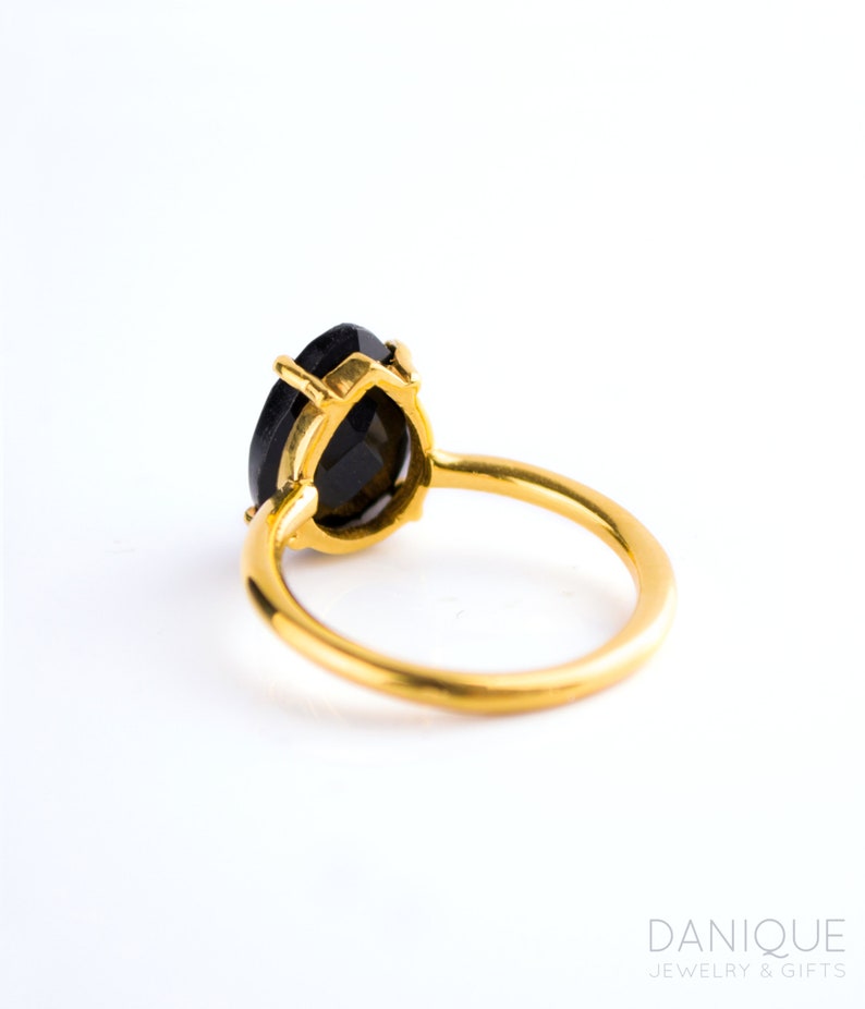 May include: A gold ring with a black pear-shaped gemstone. The ring is set with a simple band and the gemstone is set in a prong setting.