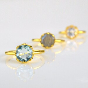 Op de afbeelding: Drie gouden ringen met verschillende edelstenen. De ring aan de linkerkant heeft een lichtblauwe edelsteen, de middelste ring heeft een grijze edelsteen en de ring aan de rechterkant heeft een heldere edelsteen.