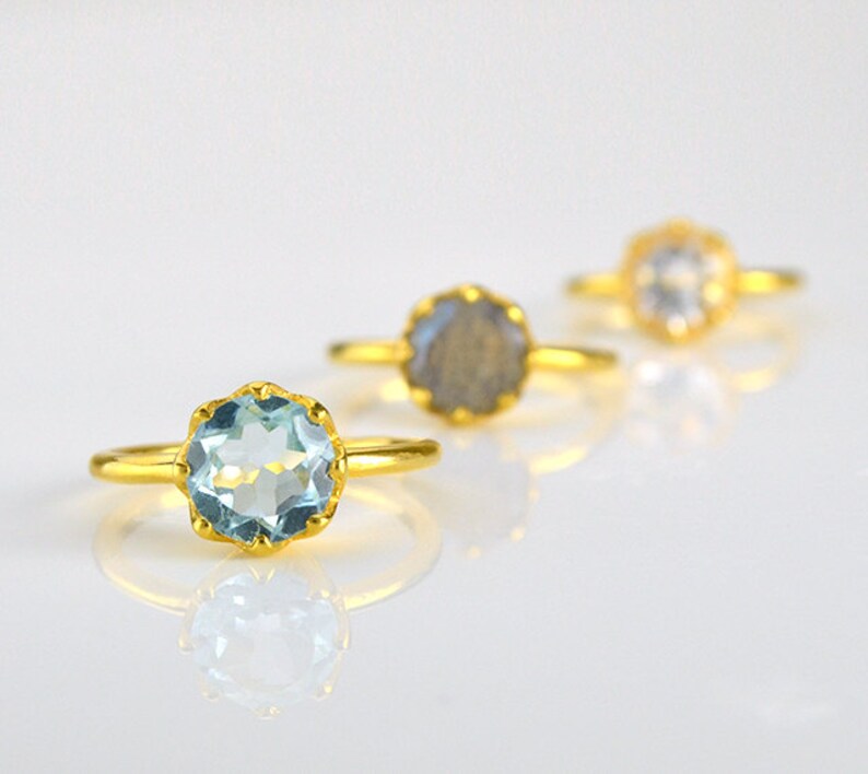 Op de afbeelding: Drie gouden ringen met verschillende edelstenen. De ring aan de linkerkant heeft een lichtblauwe edelsteen, de middelste ring heeft een grijze edelsteen en de ring aan de rechterkant heeft een heldere edelsteen.