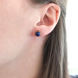 May include: A pair of gold stud earrings with a round blue gemstone.