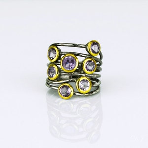 May include: A silver and gold ring with multiple bands and purple gemstones. The ring is set on a white background.