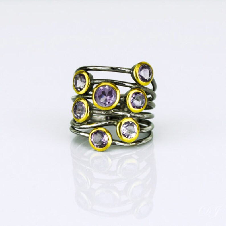 May include: A silver and gold ring with multiple bands and purple gemstones. The ring is set on a white background.