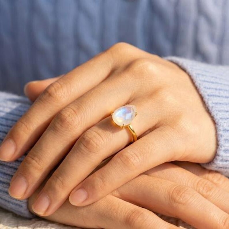 Moonstone ring worn on hand with blue sweater, showing the scale of the pear-shaped rainbow moonstone and gold band. A June birthstone ring, teardrop gemstone ring, gold moonstone ring, birthday gift for June, bridesmaid ring, or everyday statement ring.