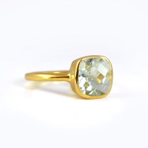 May include: A gold ring with a light green square-shaped gemstone.