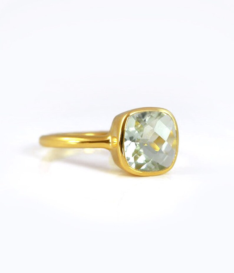 May include: A gold ring with a light green square-shaped gemstone.