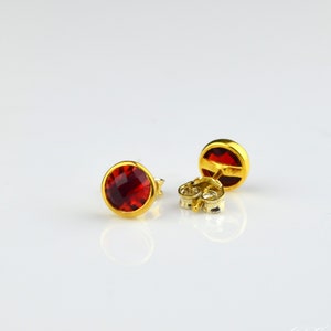 May include: A pair of gold stud earrings with red gemstone accents.