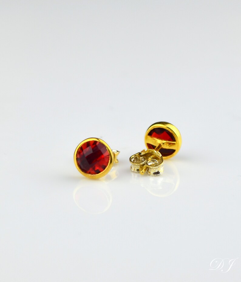 May include: A pair of gold stud earrings with red gemstone accents.