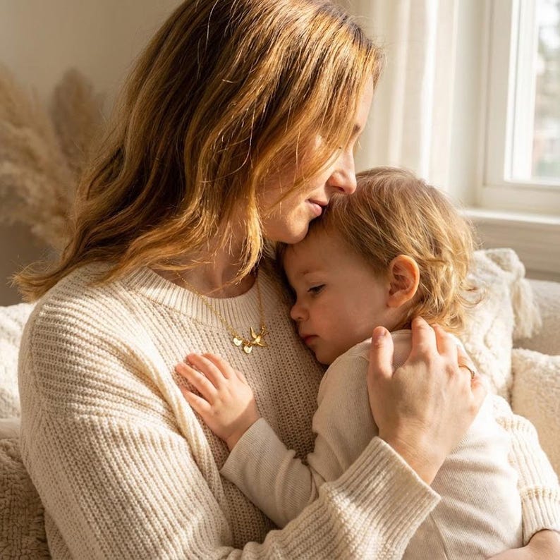 Warm lifestyle image of mother cuddling child, emotional family necklace gift idea, mama bird charm representing motherhood and growing family bond.