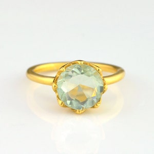Op de afbeelding: Een gouden ring met een lichtgroene edelsteen in een gegolfde zetting.
