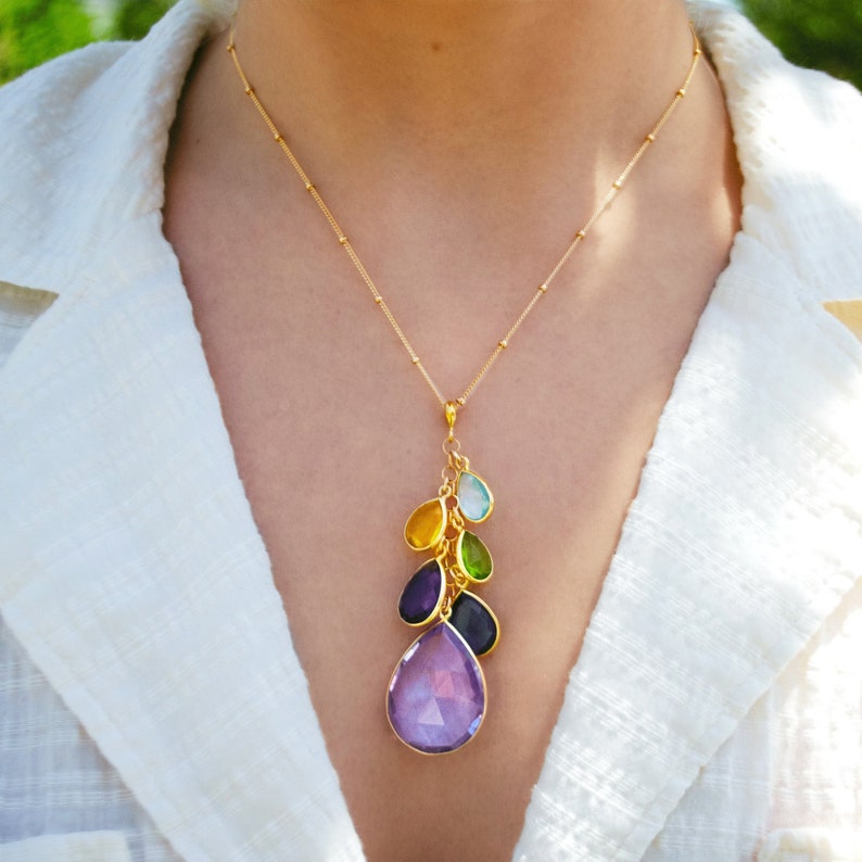 Elegant family birthstone necklace in gold vermeil featuring a cascading teardrop pendant with custom gemstones representing children, grandchildren, and loved ones. This personalized jewelry piece showcases a large purple gemstone accented by smaller yellow, green, and blue stones, symbolizing family generations. A meaningful heirloom keepsake necklace, perfect for grandma, mom, or wife as a birthday gift, anniversary jewelry, or sentimental everyday accessory.