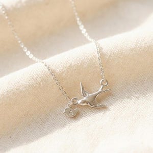 Sterling silver version on soft fabric background, minimalist bird pendant with initial baby bird charms, custom mother necklace for everyday wear.