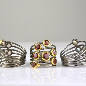 May include: Three silver rings with multiple bands and colorful gemstones. The rings are set on a white surface.