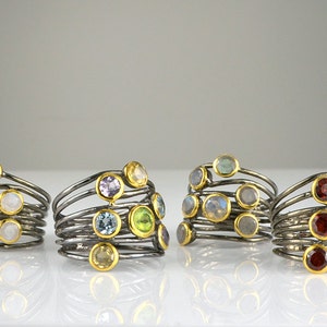 May include: Four silver rings with multiple bands and colorful gemstones. The rings feature a variety of stones, including moonstone, amethyst, aquamarine, peridot, labradorite, and garnet.