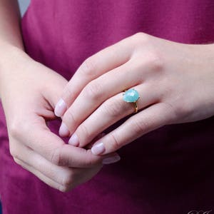 May include: A gold ring with a light blue gemstone. The ring is on a person's finger.