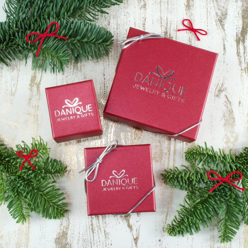 K&ouml;nnte beinhalten: Drei rote Geschenkboxen mit silbernen Schleifen. Jede Box tr&auml;gt das Logo "Danique Jewelry & Gifts", das auf der Oberseite aufgedruckt ist.
